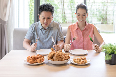 Young Asian Couples eating fried chicken together in living room of contemporary house for modern lifestyle conceptのeditorial素材
