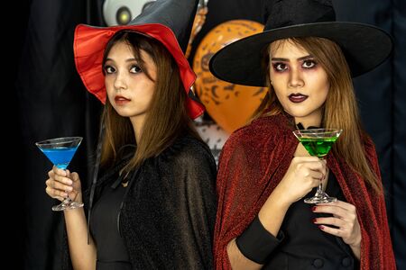 Two young adult and teenager girls celebrating a Halloween party carnival Festival in Halloween costumes drinking alcohol cocktailの写真素材