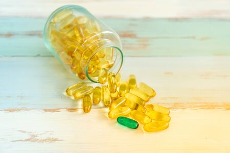 one green Pill medicine stand out from yellow pills and spilling out of pill bottle on vintage wooden backgroundの写真素材