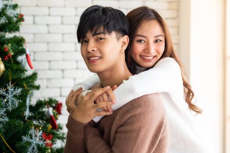 Young asian adult teenager couple hugging and  celebrateing christmas holiday together in living room with christmas tree ornament decoration.の写真素材