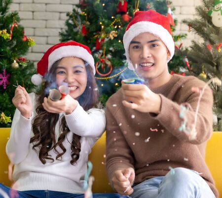 Young asian adult teenager couple celebrateing christmas holiday together with Firecrackers in living room with christmas tree decoration.の写真素材