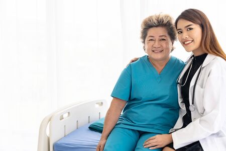 Young female doctor in uniform hugging and smiling to old elderly woman patient during a visit in hospital wardの写真素材
