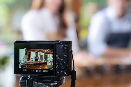 VLOG of  young adult asian owner entrepreneur review cafe coffee shop and live in social media for online marketing with camera in cafe. Using for startup of small business marketing and consumerism concept.の写真素材