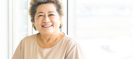 Portrait of happy and smile elderly senior adult female standing beside window in domestic living...