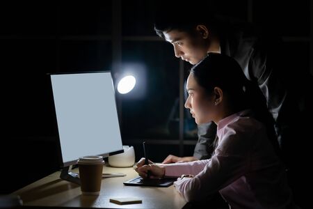 Young adult asian businessman dicuss with collegue about work late at night in their office with desktop computer. Using as hard working and working late concept.の写真素材