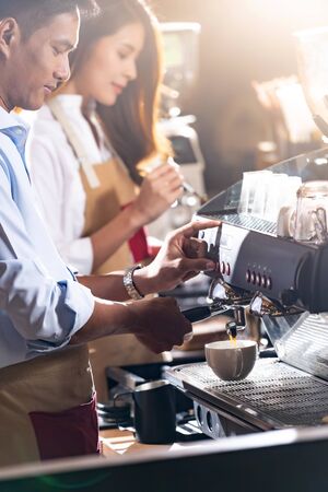 Side view shot of a barista brewing coffee by modern coffeemaker machine to making a cup of coffee with other barista working in background. Using for small business entrepreneur owner concept.の写真素材