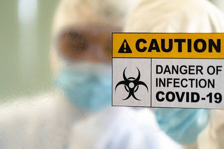 Caution danger Signage of COVID-19 coronavirus in front of Laboratory room with background of Scientists working and researching vaccine for ncov-19 virus for world pandemic situation.の写真素材