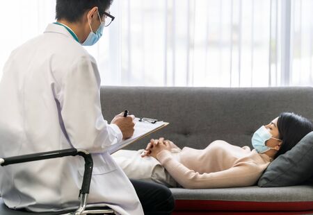 Psychotherapist doctor visting patience house working with depressed asian woman who lay on sofa in living room for consult about mental health.の写真素材