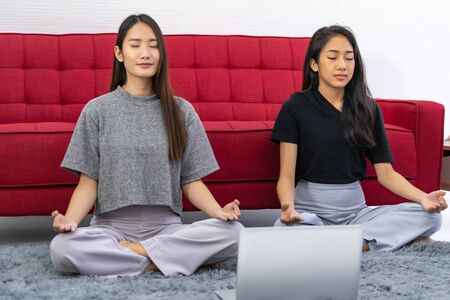 Two asian Woman do meditate from online meditation coaching to relax and reduce stress and strain for good mental health cause from city lockdown from coronavirus COVID-19 Pandemic.の写真素材