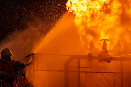 Firefighter using water fog type fire extinguisher to fighting with the fire flame from oil pipeline leak and explosion on oil rig and natural gas station. Firefighter and industrial safety concept.の写真素材