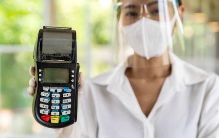 Portrait attractive asian waitress wear face mask and face shield hold credit card reader for...