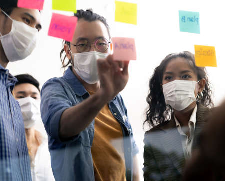 Interracial asian business team brainstorming idea at office meeting room after reopen due to coronavirus COVID-19 city lockdown. They wear face mask reduce risk to infection as new normal lifestyle.の写真素材