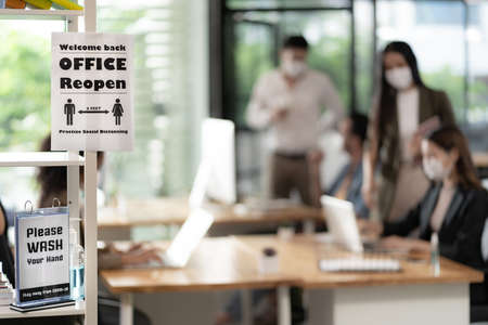 Signage of Office Reopen with social distancing practice with blurred background of Asian team business people working and wear face mask in new normal office to prevent covid-19 virus spreading.の写真素材