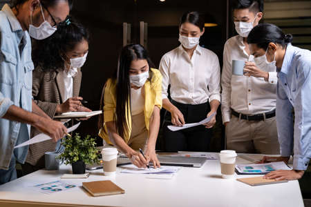 Work late concept of Interracial asian business team brainstorm idea at office meeting room at night. They wear face mask reduce risk to infection of COVID-19 coronavirus as new normal lifestyle.の写真素材