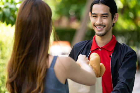 Delivery asian bike man pick up bakery grocery bag from bakery shop to deliver to customer who make online order. Food delivery service concept in new normal after coronavirus pandemic.の写真素材