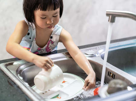 Asian girl washing her dish and tableware by herself, housework for child make executive function for kid. House-working for kid lifestyle and family concept.の写真素材