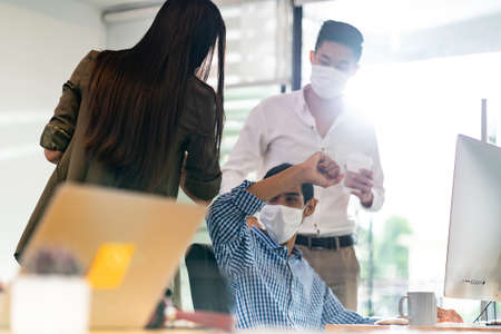 Businessperson do alternative greeting in new normal office lifestyle. They wear protective face mask and use elbow touch instead of hand shake to reduce infection of coronavirus COVID-19.の写真素材