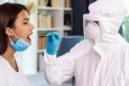 Medical staff with PPE suit test coronavirus covid-19 to asian woman by throat swab at home.