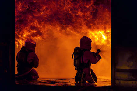 Firefighters using water fog fire extinguisher to fighting with the fire flame in large building. Firefighter and industrial safety disaster and public service concept.の写真素材