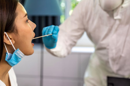 Medical staff with PPE suit test  covid-19 to asian woman by throat swab at home.
