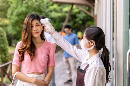 Asian waitress with face mask taking temperature to customer before getting in restaurant with social distance queue in line. New normal restaurant concept after coronavirus covid-19 pandemic.の写真素材