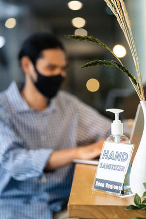 Signage of Hand Sanitizer around office for hygiene practice after reopen with blurred background of business people working and wear face mask in new normal office to prevent covid-19 virus spreadingの写真素材