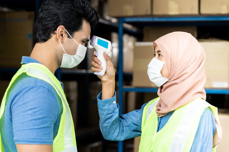 Islam asian warehouse worker taking temperature to worker before getting in factory after reopening...