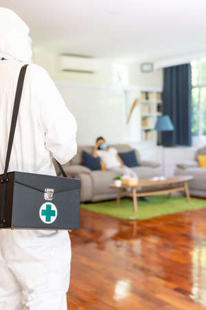 Close up medical staff in personal protective equipment PPE suit with background of asian woman with face mask waiting in living room of apartment .Delivery coronavirus covid-19 test at home concept.の写真素材