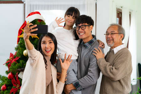 Multigenerational asian Family ,Mom Dad daughter girl and grandfather ,selfie with a Christmas tree after decorate the Christmas ornament prepare season greeting of Merry Christmas and Happy Holidays.の写真素材