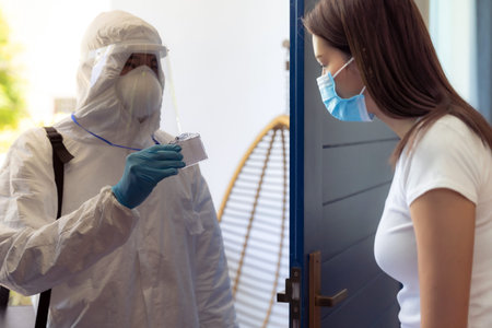 Medical staff in PPE suit show his ID card to patient to identified himself at home before doing...
