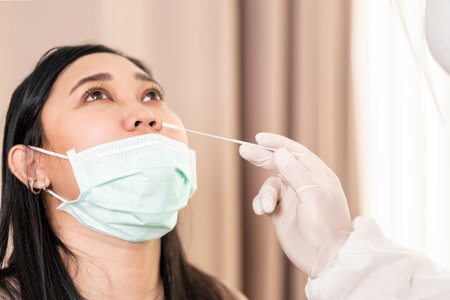 Medical staff with PPE suit test coronavirus covid-19 to asian woman by nose swab at hospital. COVID-19 testing health care concept.の写真素材