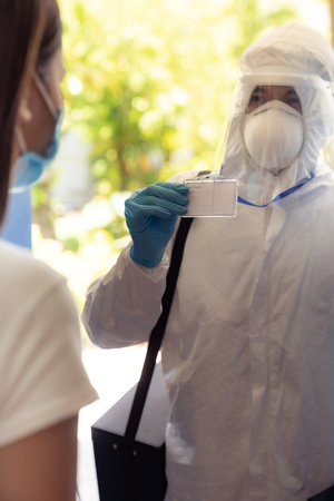 Medical staff in PPE suit show his ID card to patient to identified himself at home before doing swab for COVID-19 at home delivery. Delivery coronavirus covid-19 test at home concept.の写真素材