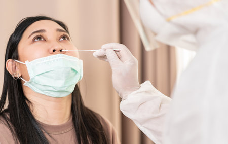 Medical staff with PPE suit test coronavirus covid-19 to asian woman by nose swab at hospital. COVID-19 testing health care concept.の写真素材
