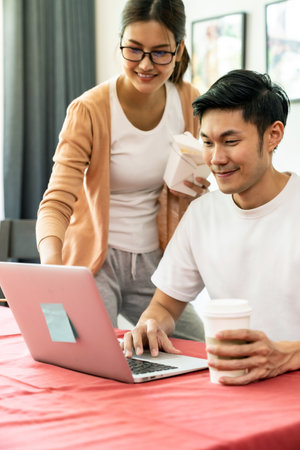 Asian couple work from home in the dining room with delivery take away food box while city lockdown from coronavirus covid-19 pandemic. New Normal lifestyle working from home.の写真素材