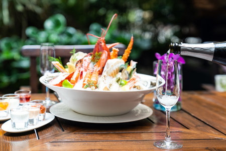 Waiter pouring white wine into wine glass and serving to customer in restaurant with big bowl seafood on ice in background. Restaurant gastronomy food and drink consumerism concept.の写真素材