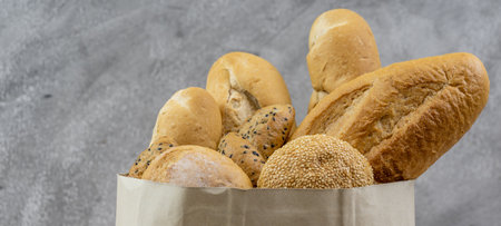 Variety bread in disposable paper bag on grey vintage loft background. Bakery food and drink and grocery concept for delivery. Panoramic web banner crop.の写真素材