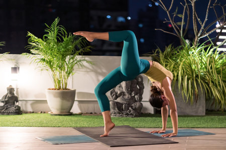 Asian female woman in sportswear bra pants practicing yoga during city lockdown alone in her apratment with background of cityscape illumination at night. Work out fitness healthy lifestyle concept.の写真素材