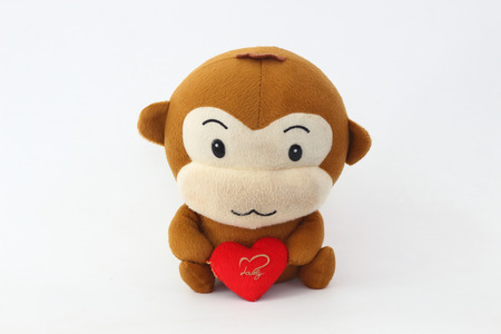 Stuffed brown monkey holding a red heart on a white background.の写真素材