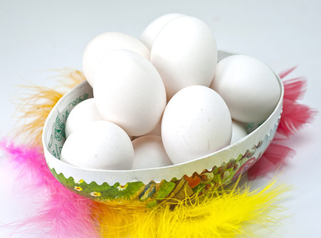 White eggs in an Easter egg surrounded by colorful feathers