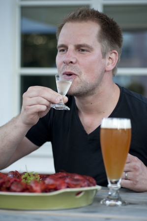A male person enjoying a schnapps togehter with some crawfish.の写真素材