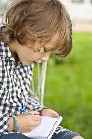 Young boy sitting oudoors drawing in a notepad の写真素材