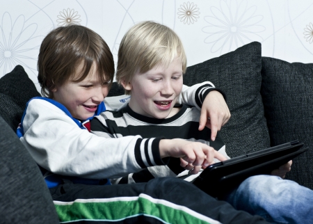 Two young kids in a sofa having fun together with a tabletの写真素材