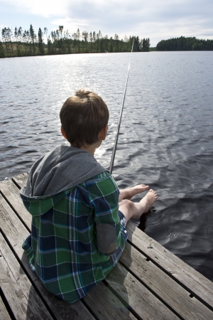 Young boy on bridge angling in a lake の写真素材