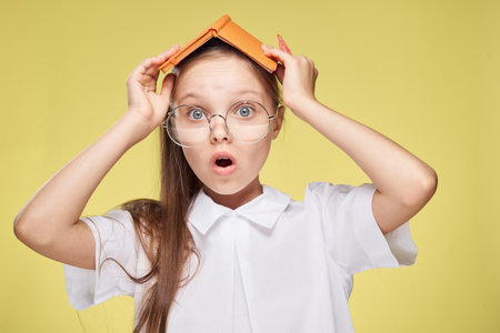 schoolgirl with textbook in hands learning childhood yellow background