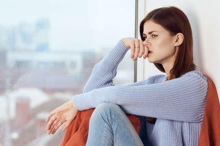 woman with sad expression sits by the window with a plaidの写真素材