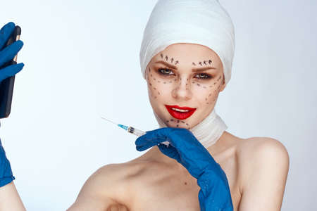 woman in blue gloves syringe in hands contour on the face lifting light backgroundの写真素材