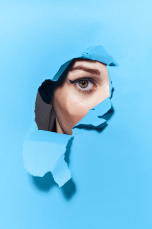 woman peeping through the holes in the poster blue studio backgroundの写真素材