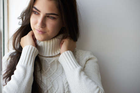 sad woman near the window in a white sweater lonelinessの写真素材