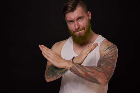 bearded man with tattoos on his arms gesturing with his hands dark background