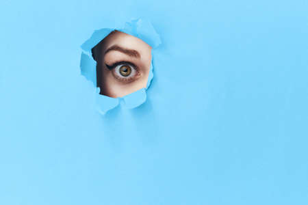 woman peeping through the holes in the poster blue studio backgroundの写真素材